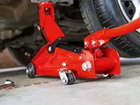 Ein roter Wagenheber hebt ein Auto auf einer Betonwerkstattfläche neben einem Autoreifen an.