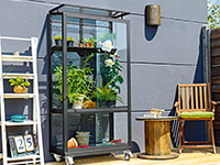Ein mobiles Glashaus mit Pflanzen steht auf einer Terrasse.