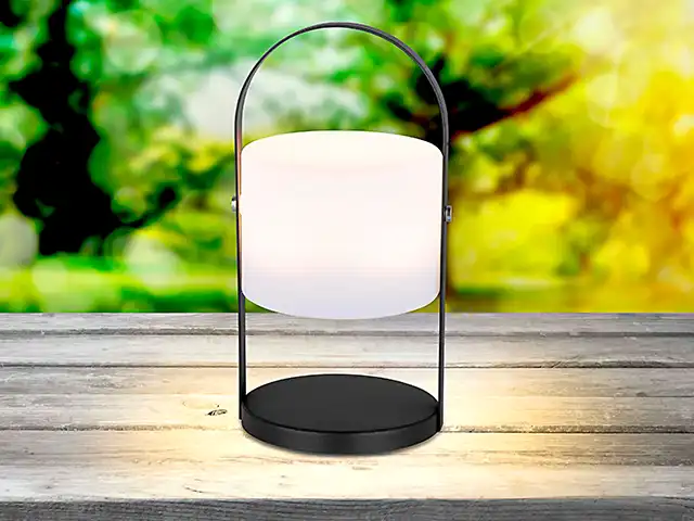 Eine schwarze Laterne leuchtet auf einem Holztisch.