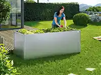 Eine Person pflegt einen Hochbeetgarten in einem gepflegten Garten mit Rasen und Hecken.