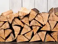 Holzscheite sind vor einer weißen Holzwand gestapelt.