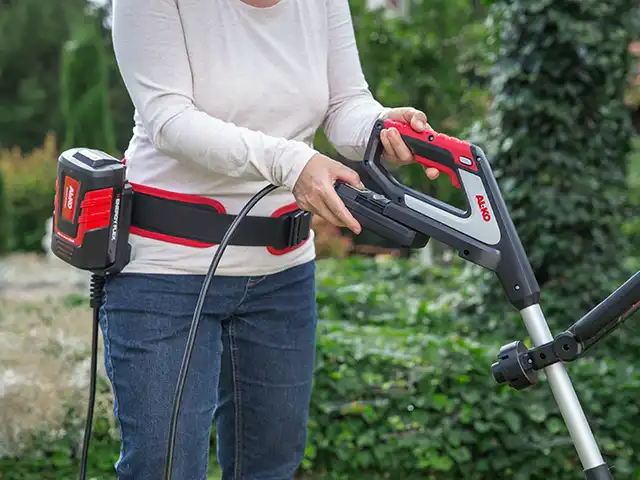 Eine Person bedient einen elektrischen Rasentrimmer mit Gürtelakku von AL-KO im grünen Garten.