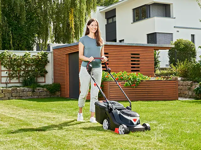 Eine Frau mäht den Rasen mit einem AL-KO Rasenmäher.