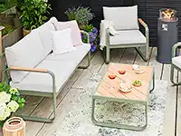 Ein modernes weißes Gartenset mit Sofa und Stühlen steht auf einer Holzterrasse, umgeben von Pflanzen.