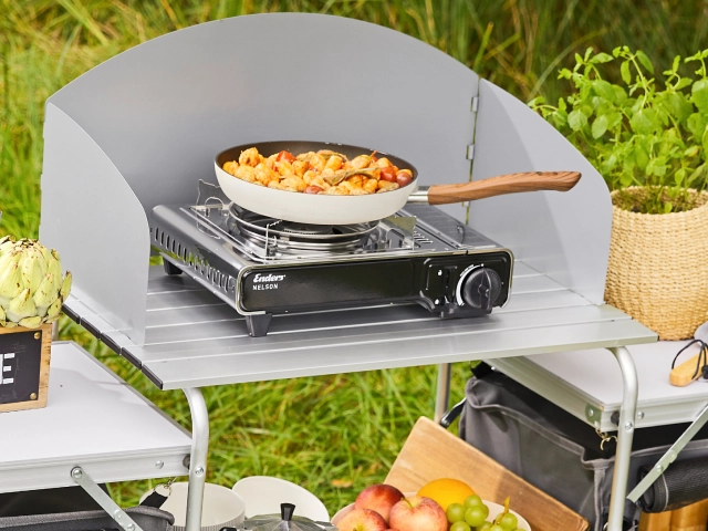 Gaskocher mit einer Pfanne auf einem Campingschutz mit Spritzschutz