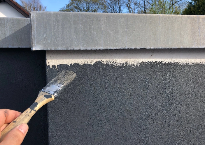 Eine Wand wird mit einem Pinsel grau gestrichen