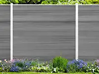 Ein grauer Zaun steht hinter blühenden Pflanzen im Garten, umgeben von grüner Vegetation.