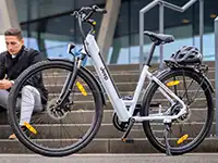 Ein silbernes E-Bike steht vor der Treppe eines modernen Gebäudes.