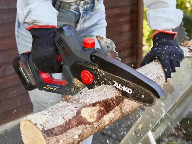 Eine Person schneidet mit einer Kettensäge von AL-KO einen Holzstamm im Freien.