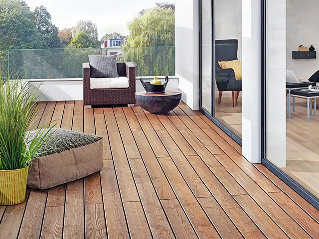 Ein Pflanzentopf steht auf einer modernen Holzterrasse neben einem gemütlichen Sitzbereich mit Kissen.