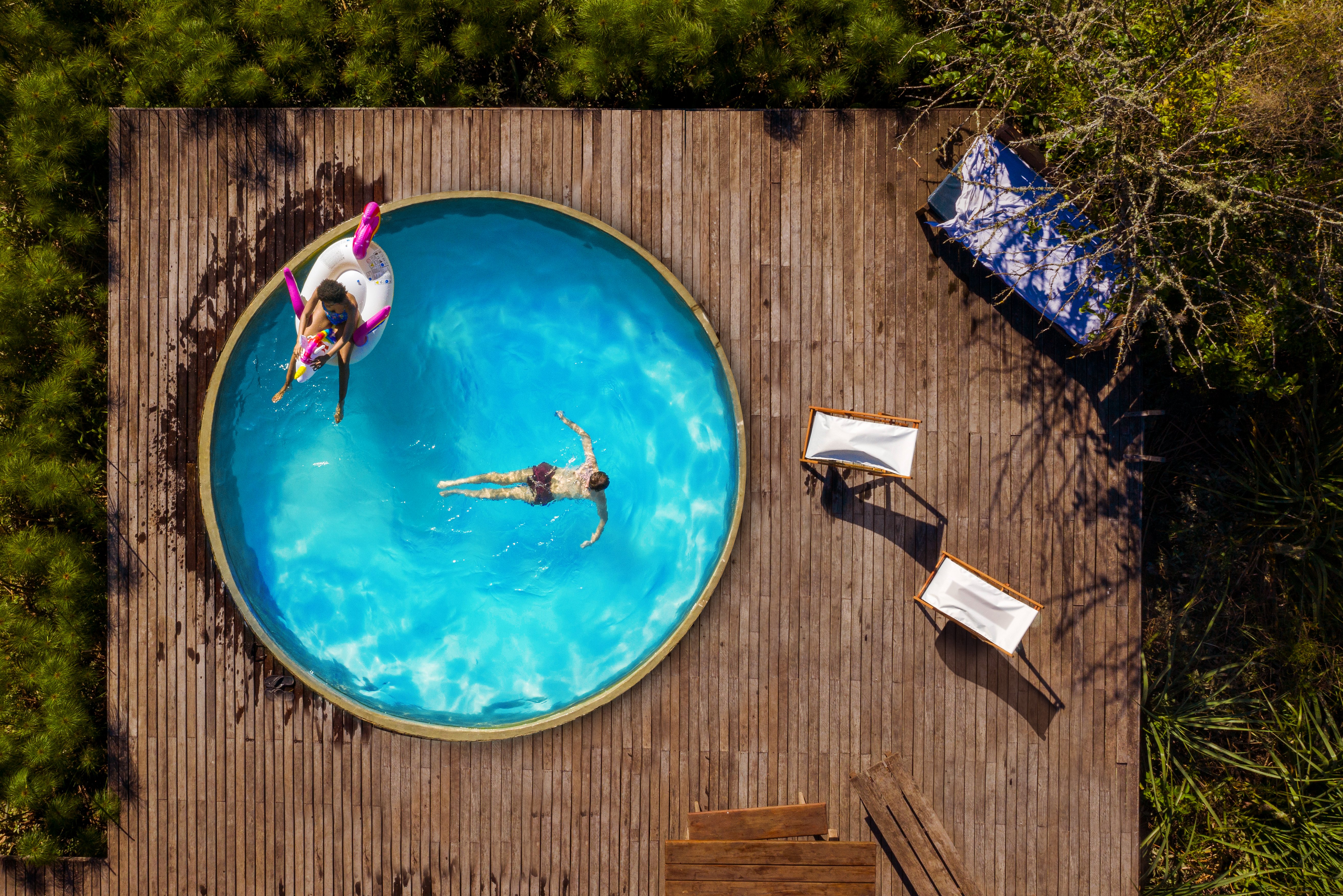Pool der auf einer Holzterrasse ist aus der Vogelperspektive mit zwei Menschen drin