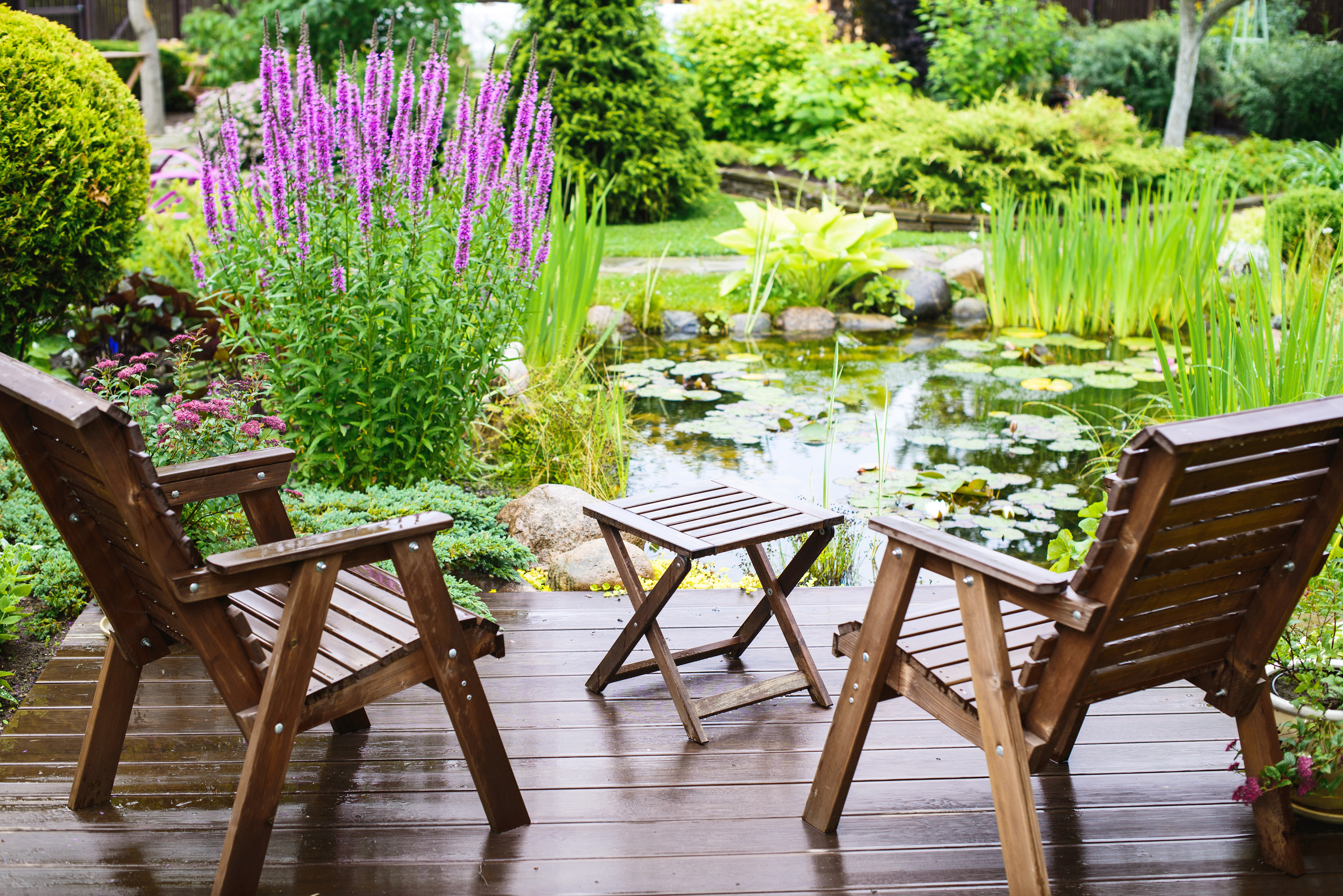 Gartenmöbel aus Holz auf einer Holzterrasse mit Blick zum Gartenteich