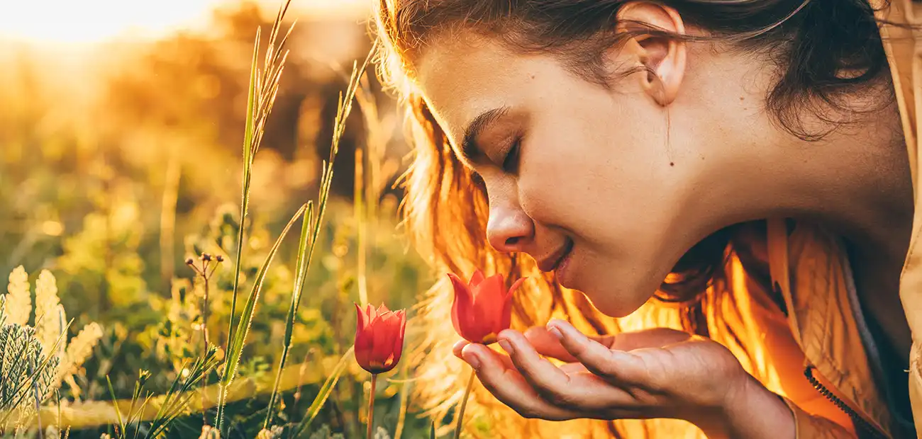 Eine Frau riecht an roten Blumen auf einer Wiese bei Sonnenuntergang.