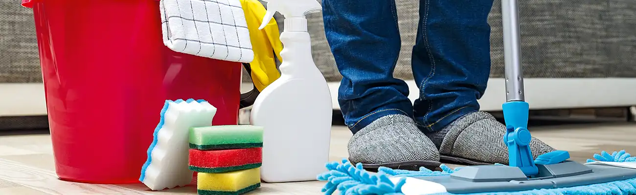 Ein Eimer mit Putzutensilien steht neben einer Person, die den Boden wischt.