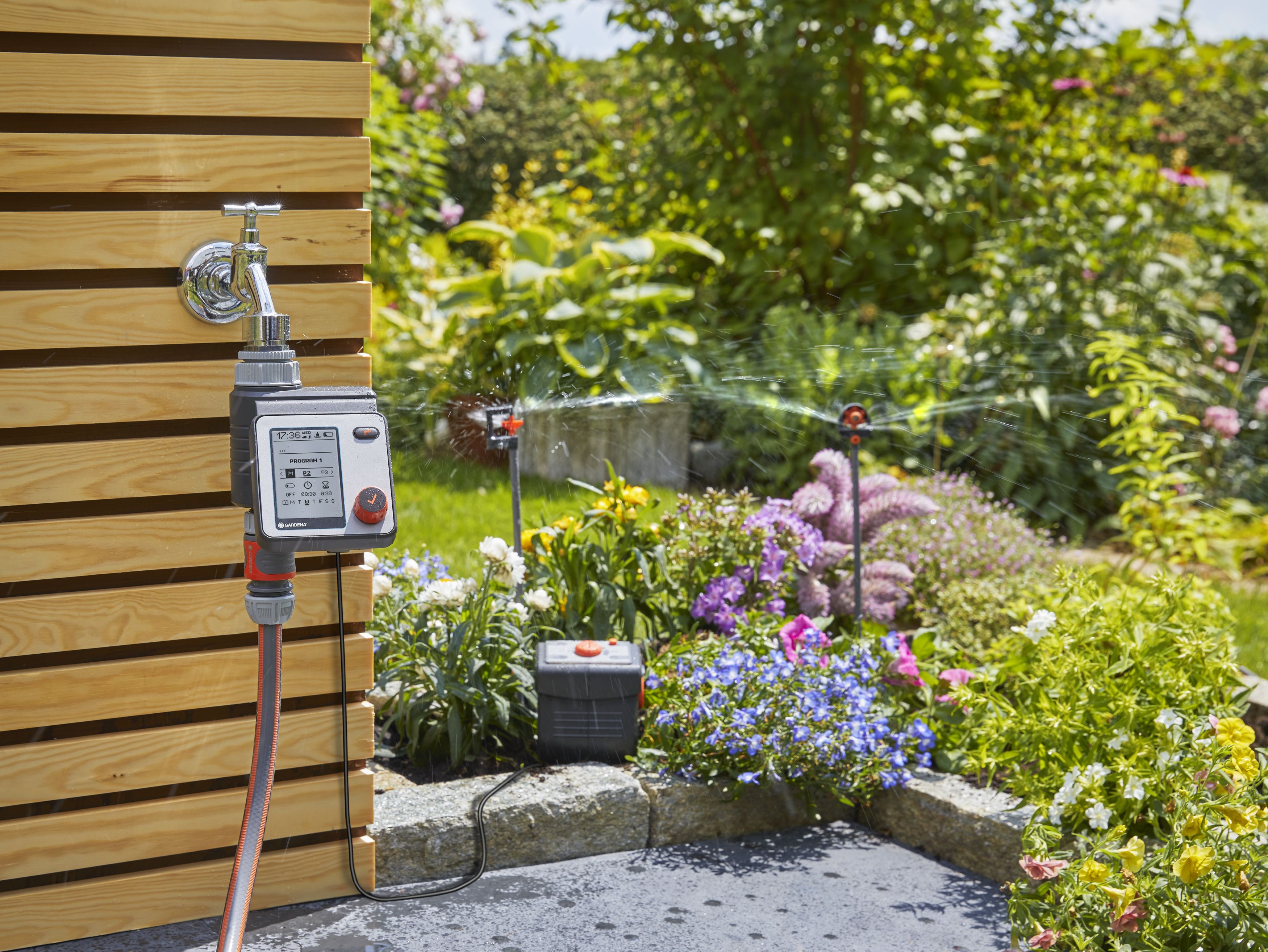 Ein Gardena Bewässerungssystem gießt bunte Blumen im Garten; ein Timer ist am Wasserhahn angeschlossen.