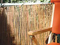 Ein oranger Stuhl steht neben einem Sichtschutz aus Schilfrohr auf einem Balkon.