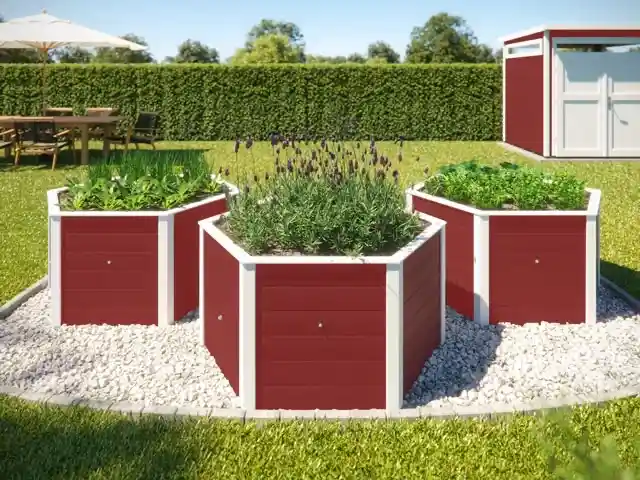Drei rote, sechseckige Hochbeete mit Pflanzen stehen auf Kies im Gartenbereich.