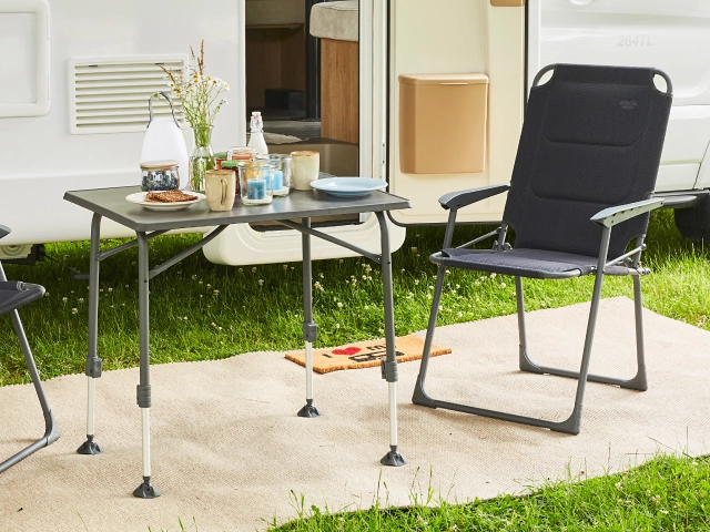 Gedeckter Campingtisch mit Campingstuhl vor Wohnwagen