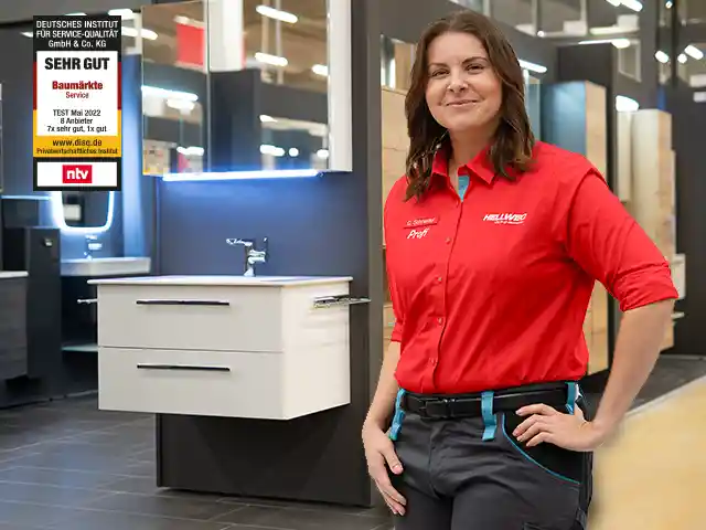 Eine lächelnde Hellweg Mitarbeiterin steht im Baumarkt neben einem Waschbecken.