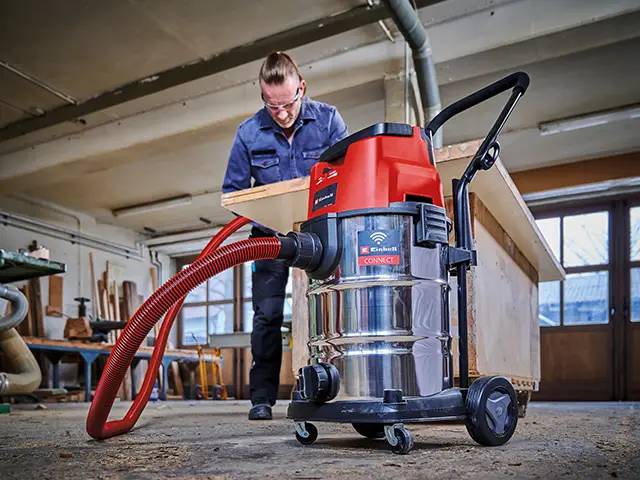 Ein Mann saugt mit einem Einhell Nass-Trockensauger den Staub in einer Werkstatt auf.