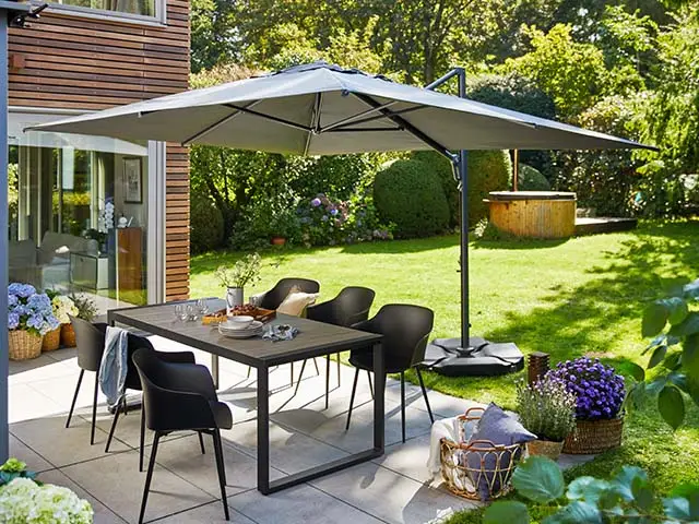 Ein Tisch mit Stühlen steht unter einem Sonnenschirm auf einer Terrasse im Garten.