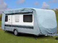 Ein Wohnwagen ist mit einer Abdeckplane auf einer grünen Wiese unter blauem Himmel abgestellt.