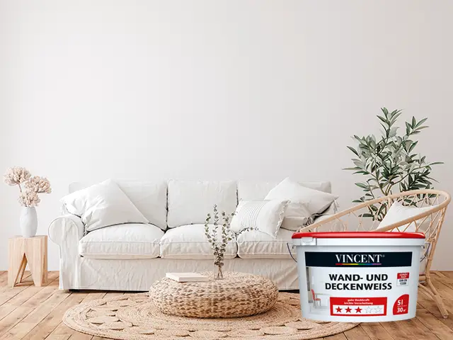 Ein weißer Farbeimer steht in einem hellen Wohnzimmer mit Sofa und Pflanzen.