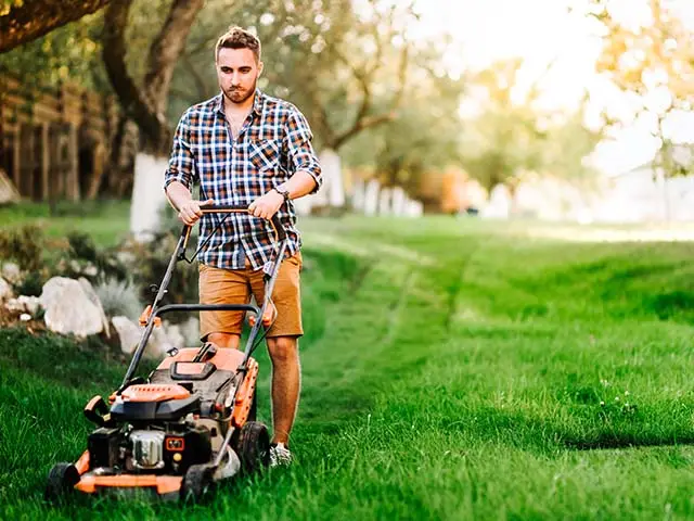 Ein Mann schiebt einen Rasenmäher über eine grüne Rasenfläche im Garten.