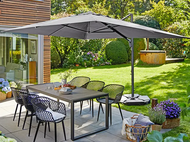 Ein großer Sonnenschirm steht über einem Esstisch mit sechs Stühlen in einem Garten.