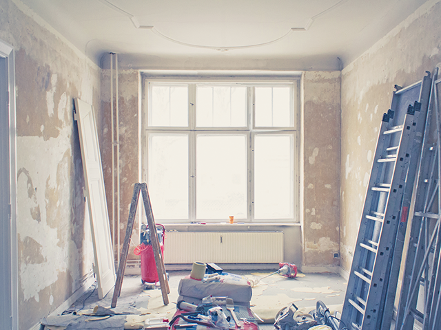 Eine Leiter steht in einem renovierungsbedürftigen Raum mit einem großen Fenster.