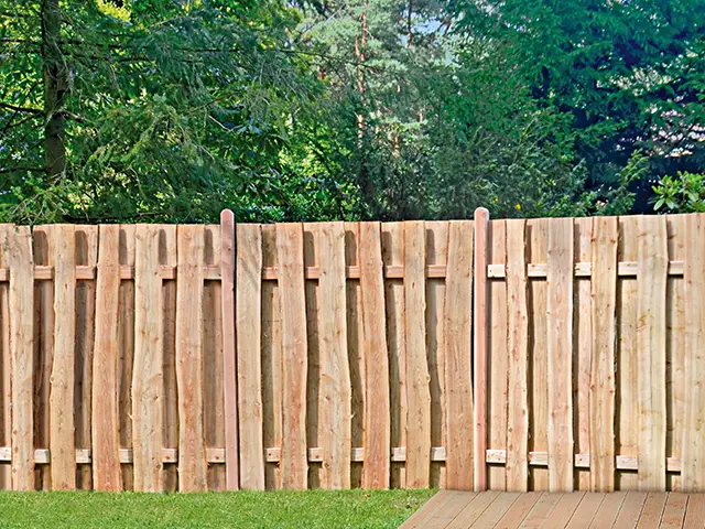 Ein hölzerner Zaun steht still im Garten, umgeben von dichten grünen Bäumen.