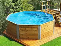 Ein achteckiger Holzpool steht auf einer Terrasse, umgeben von grünen Bäumen und Rasen.