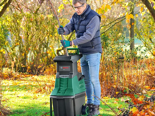 Ein Mann zerkleinert Äste mit einem Bosch-Häcksler im herbstlichen Garten.