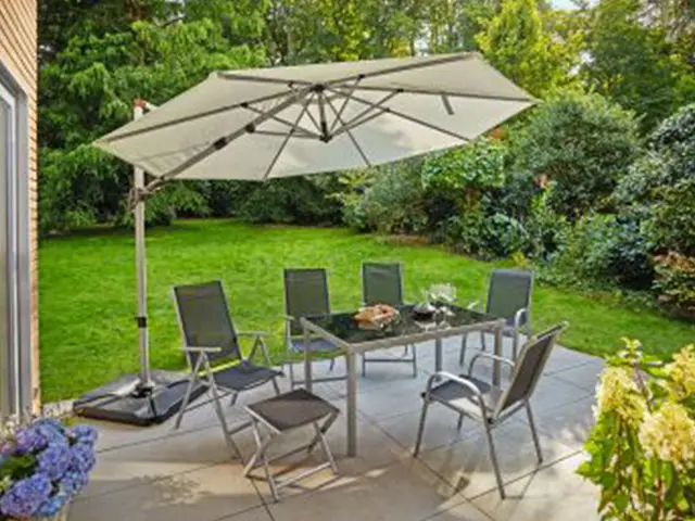 Ein Garten mit Sitzgruppe, großem Sonnenschirm, Tisch und grüner Rasenfläche im Hintergrund.