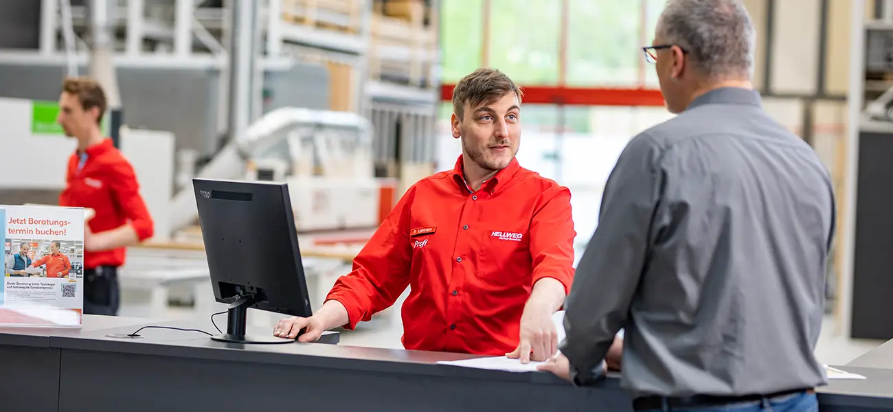 Ein Mitarbeiter berät einen Kunden an einem Tresen in einem Hellweg Baumarkt.