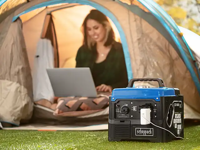 Ein tragbarer Generator lädt ein Gerät vor einem Zelt, in dem eine Person sitzt.