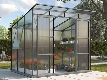 Ein Gewächshaus mit Pflanzen im Inneren steht in einem sonnigen Garten.