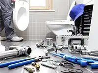 Werkzeuge liegen auf dem Badezimmerboden, während ein Klempner an der Toilette arbeitet.