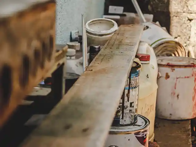 Ein Holzbrett liegt auf mehreren bunten Farbeimern in einem Werkstattbereich.