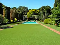 Ein Pool liegt in einem gepflegten Garten, umgeben von hohen Bäumen und Rasen.