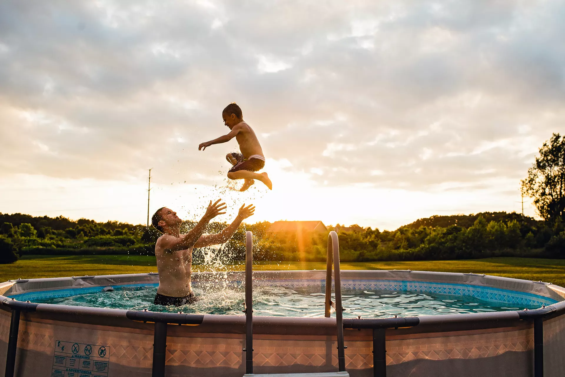Ein Mann wirft im Garten bei Sonnenuntergang ein Kind im Schwimmbecken in die Luft.