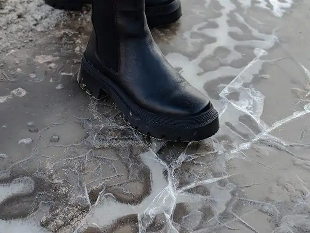 Ein schwarzer Stiefel steht auf einem gefrorenen, rissigen Straßenbelag.