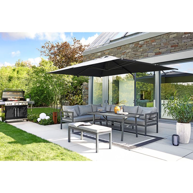 Eine moderne Terrasse mit grauem Sofa-Set und großem Sonnenschirm in einem grünen Garten.