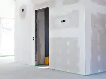 Eine unfertige Trockenbauwand mit Türöffnung steht in einem hellen, leeren Raum.