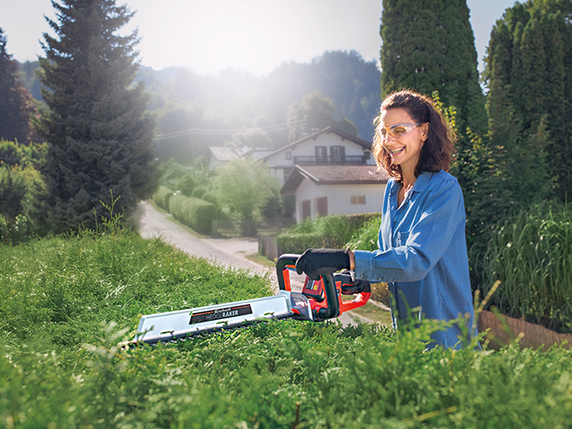 Frau mit Heckenschere und Schutzbrille schneidet Hecke
