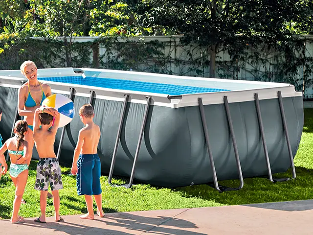 Eine Frau und Kinder spielen mit einem Ball neben einem großen Pool im Garten.