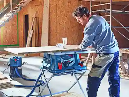 Ein Mann führt Schreinerarbeiten auf einer Werkbank in einer Baustellenumgebung aus.
