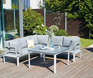 Ein graues Gartensofa steht auf einer Holzterrasse, umgeben von Pflanzen und Glaswänden.