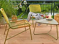 Auf einer Terrasse stehen gelbe Stühle neben einem Tisch mit Getränken im Freien.