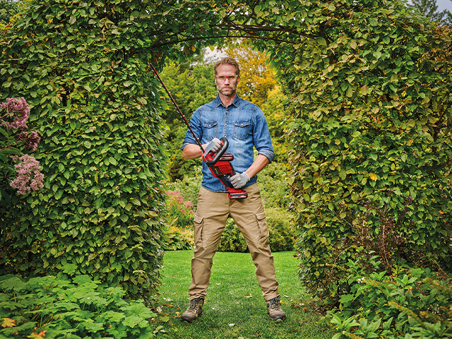 Mann mit Heckenschere vor Hecke mit Torbogen